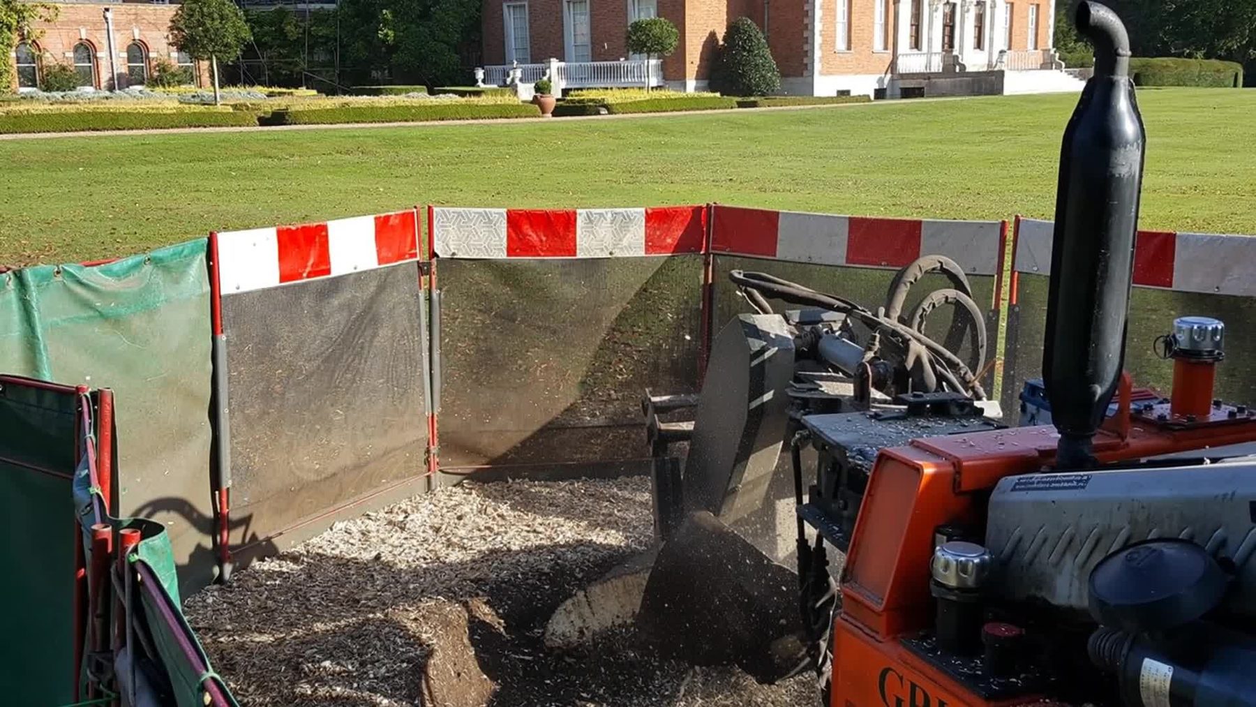 Tracked stump grinder working behind red and white safety screens