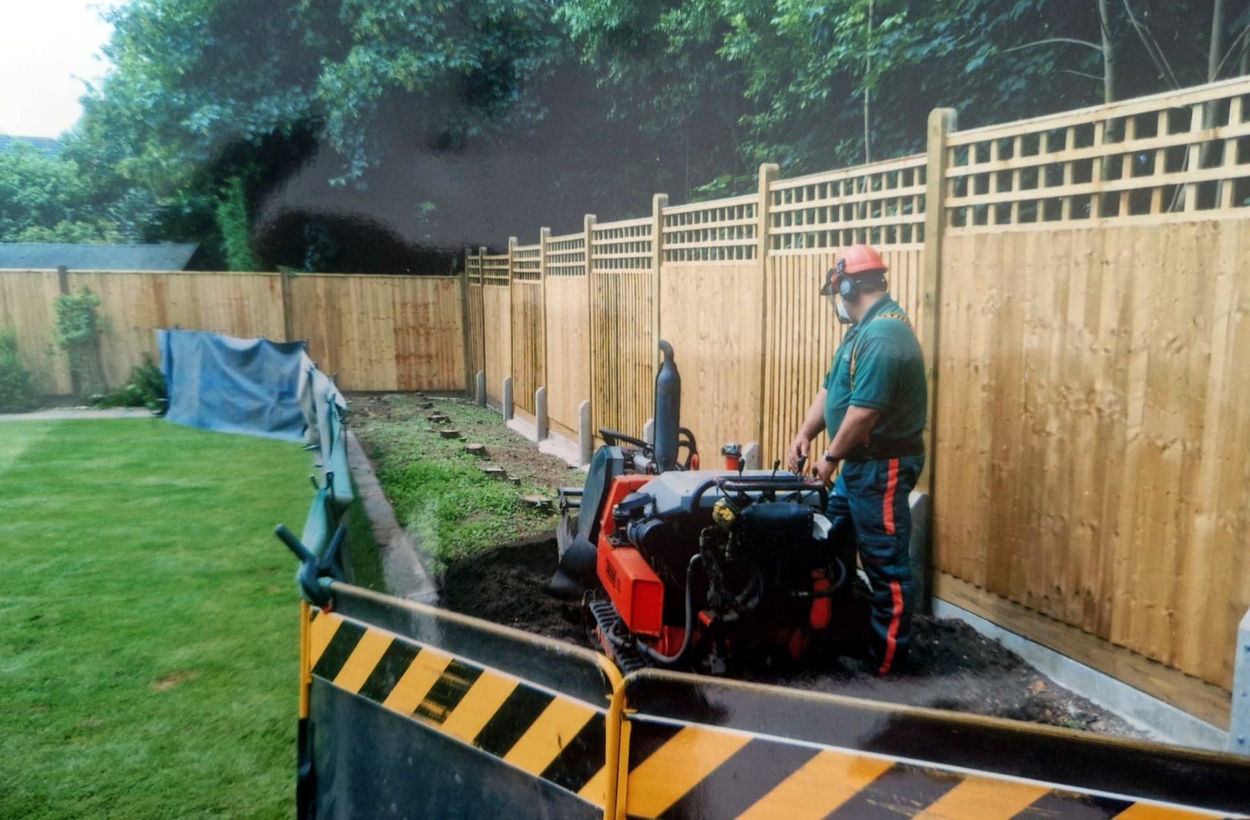 Grinding stumps along a new garden fence line with screens protecting the lawn