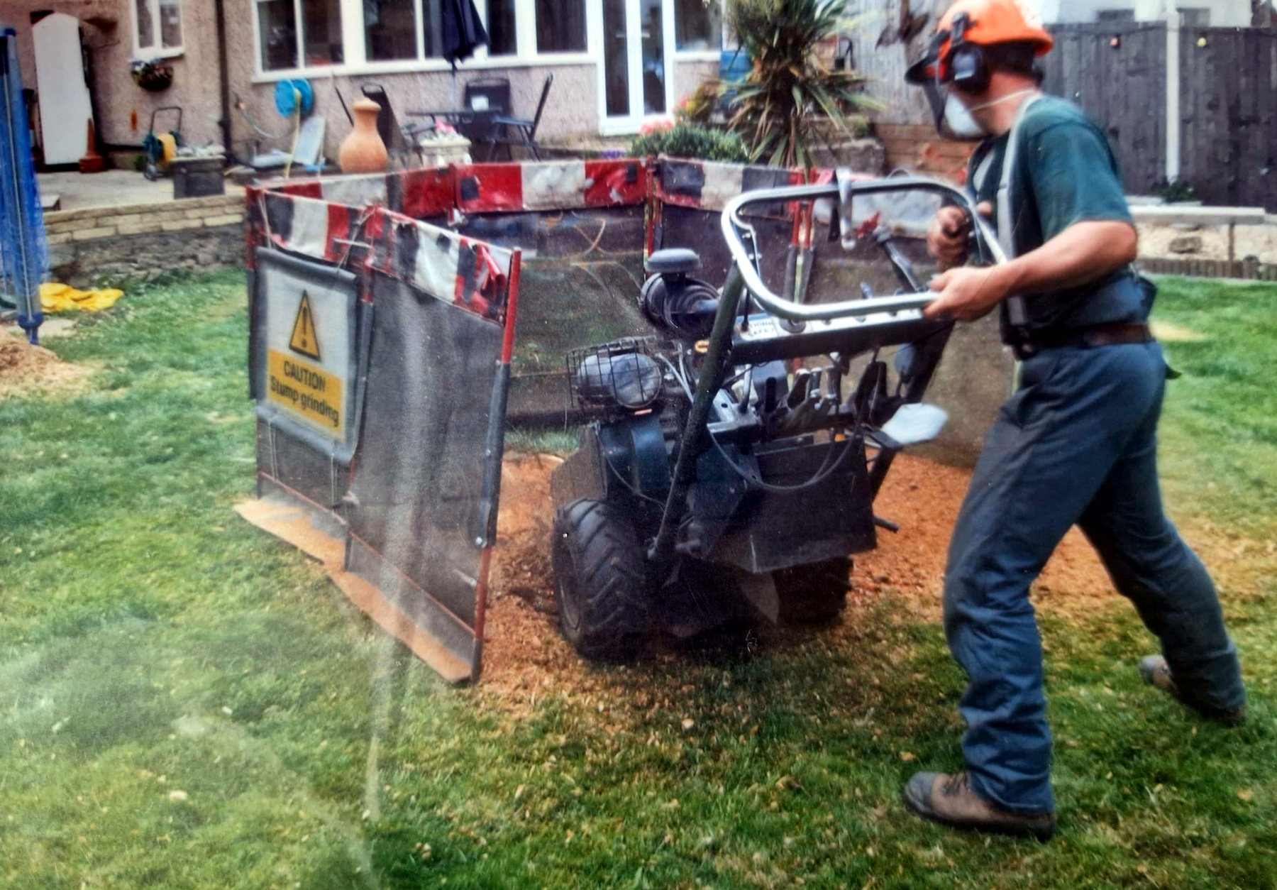 Small stump grinder at work behind safety screens on a back garden lawn