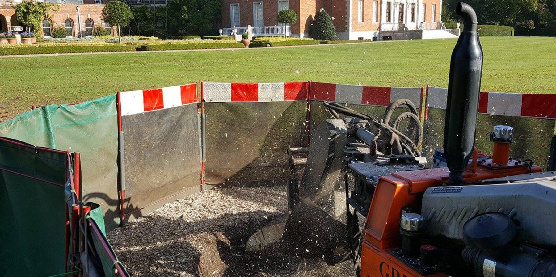 Green & Co grinding a stump behind safety screens on the lawn of a stately home in Kent